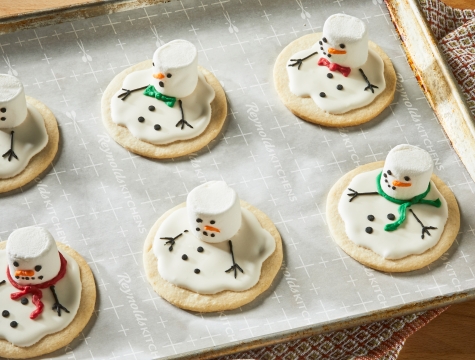 Melted snowman sugar cookies on a parchment lined baking sheet