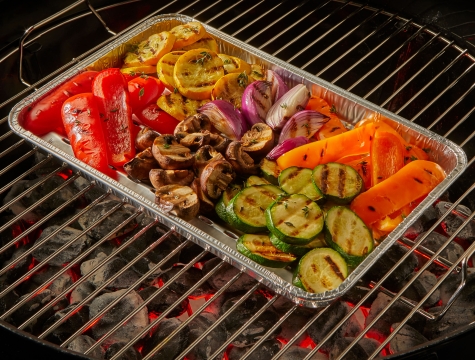 Roasted veggies sitting on a grill pan on a charcoal grill