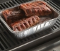 Disposable pan filled with ribs sitting on a grill