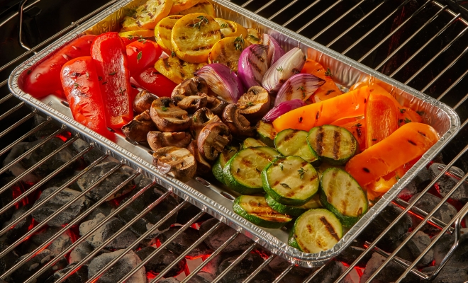 Grill pan sitting on a charcoal grill topped with roasted vegetables