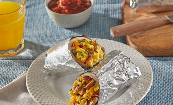 Breakfast burrito wrapped in a foil sheet and sitting on a plate