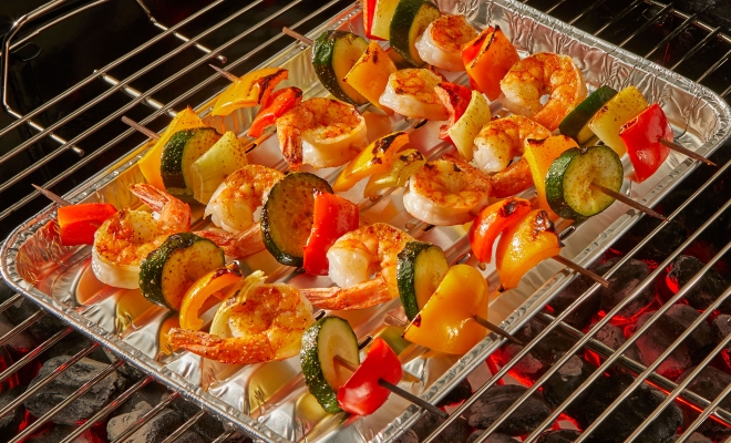 Shrimp and vegetable skewers sitting on top of a grill pan on a charcoal grill