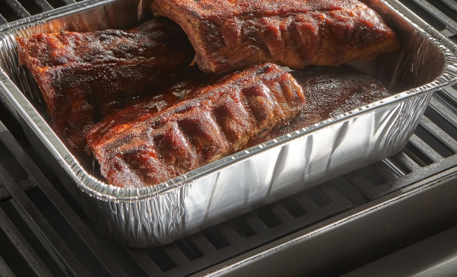 Disposable pan filled with ribs sitting on a grill