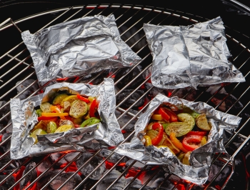 Foil packets sitting on a charcoal grill filled with roasted vegetables
