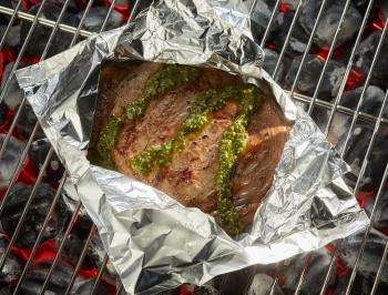meat topped with pesto in a grill packet on the grill