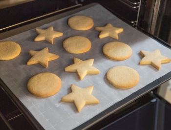 Star and circle shaped sugar cooking on a parchment lined baking sheet sitting on an oven grate