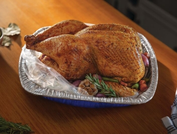 Roasted turkey in a disposable roasting pan half covered in an oven bag