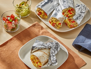 Breakfast burritos wrapped in aluminum foil sitting on a plate on a kitchen table