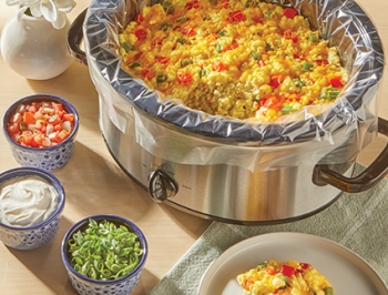 Egg casserole in a slow cooker lined with a slow cooker liner and surrounded by a variety of toppings