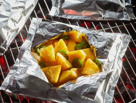 Pineapple and jalapenos in an open foil packet on a hot grill