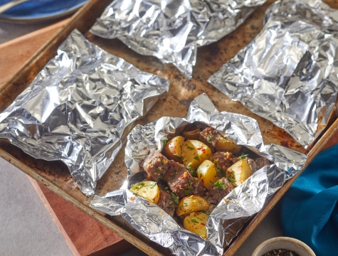 Baking sheet topped with aluminum foil packets with roasted potatoes inside.