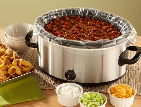 chili in a slow cooker lined with a Reynolds Kitchens slow cooker liner sitting alongside small bowls of toppings