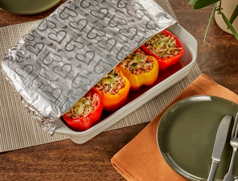 Stuffed peppers in a white ceramic baking dish partially covered with Reynolds Wrap Fun Foil with embossed heart design