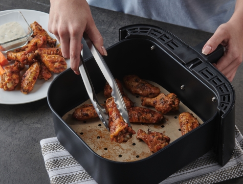 person removing chicken wings from an air fryer basket lined with a Reynolds Kitchens Air Fryer Liner