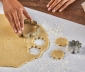 person using a cookie cutter to shape cookie dough that is rolled and sitting on a sheet of countertop prep paper