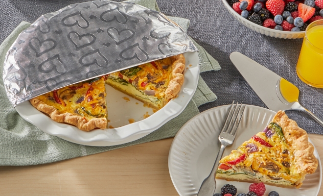 Quiche in a white ceramic pan with one slice removed partially covered in Reynolds Wrap Fun Foil with embossed heart design