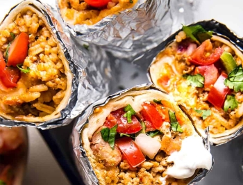 burritos filled with rice, tomatoes, cilantro and sour cream partially wrapped in aluminum foil