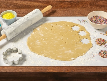 cookie dough sitting on a sheet of Reynolds Kitchens Countertop Prep Paper alongside a rolling pin, cookie cutter, sprinkles and frosting