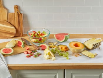 Fruit salad being prepared on a wood countertop covered in Reynolds Kitchens Countertop Prep Paper